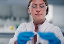 Young adult woman wearing safety glasses and lab coat, holding test tube while performing science research in a chemistry lab