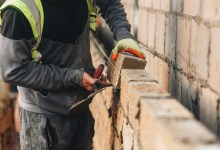 Bricklayer constructing stone wall using stone blocks, cement mortar mix and trowel