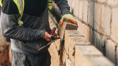 Bricklayer constructing stone wall using stone blocks, cement mortar mix and trowel