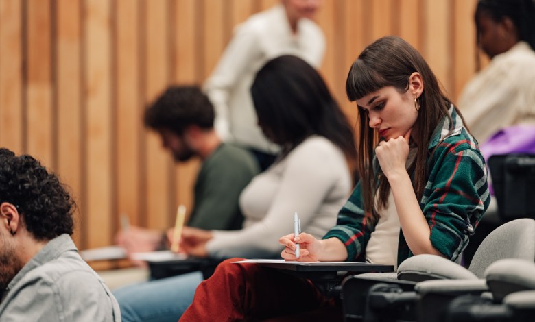 Students sitting in a modern lecture hall, writing papers and learning. An instructor is walking through the aisles