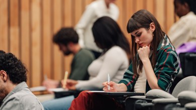 Students sitting in a modern lecture hall, writing papers and learning. An instructor is walking through the aisles